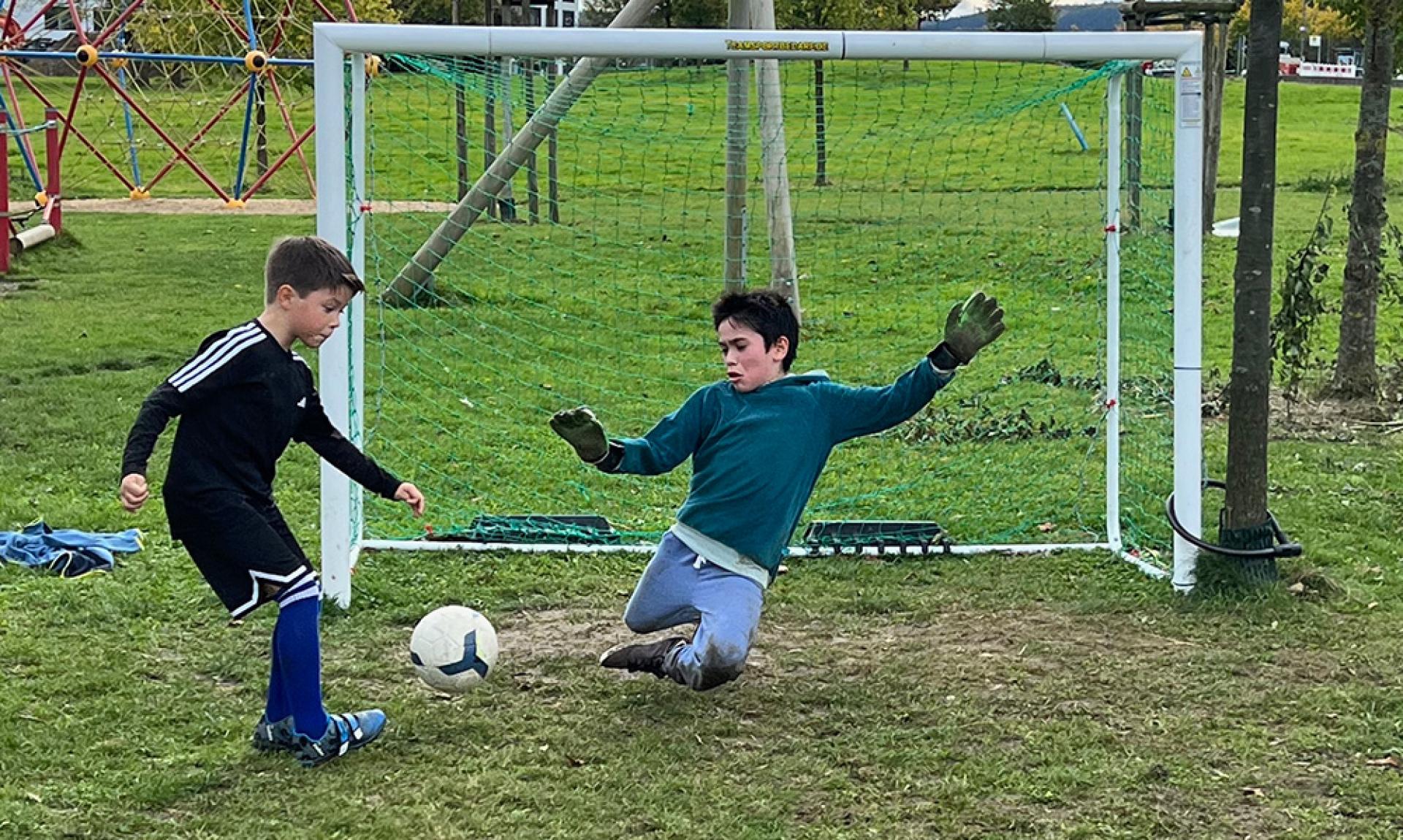 Zwei Jungen sind aktiv beim Fußballspielen auf einem Sportplatz zu sehen