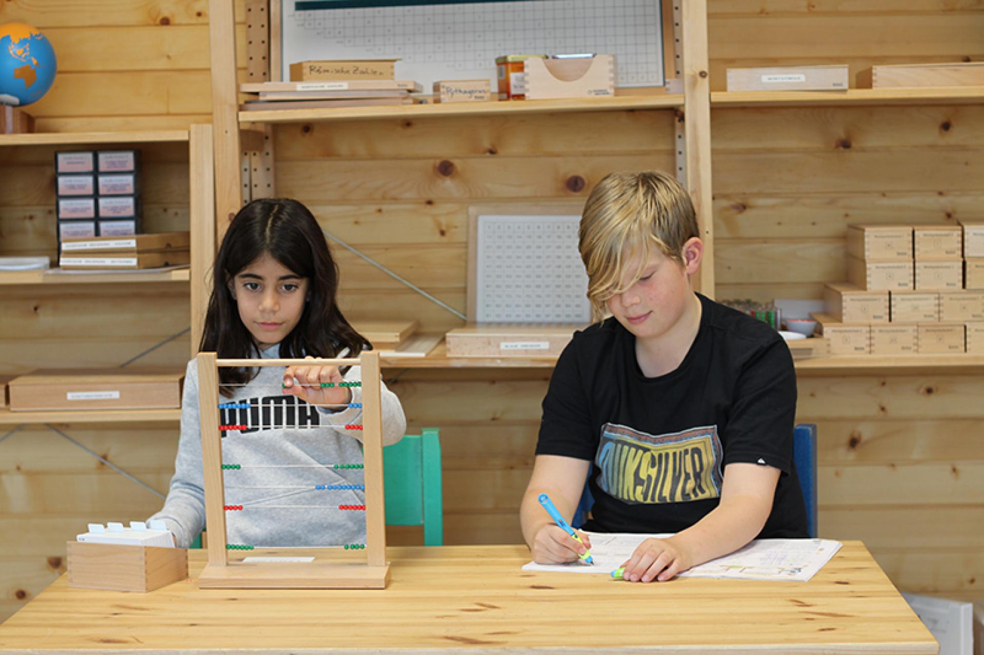Zwei Kinder sitzen an einem Holztisch und lernen gemeinsam