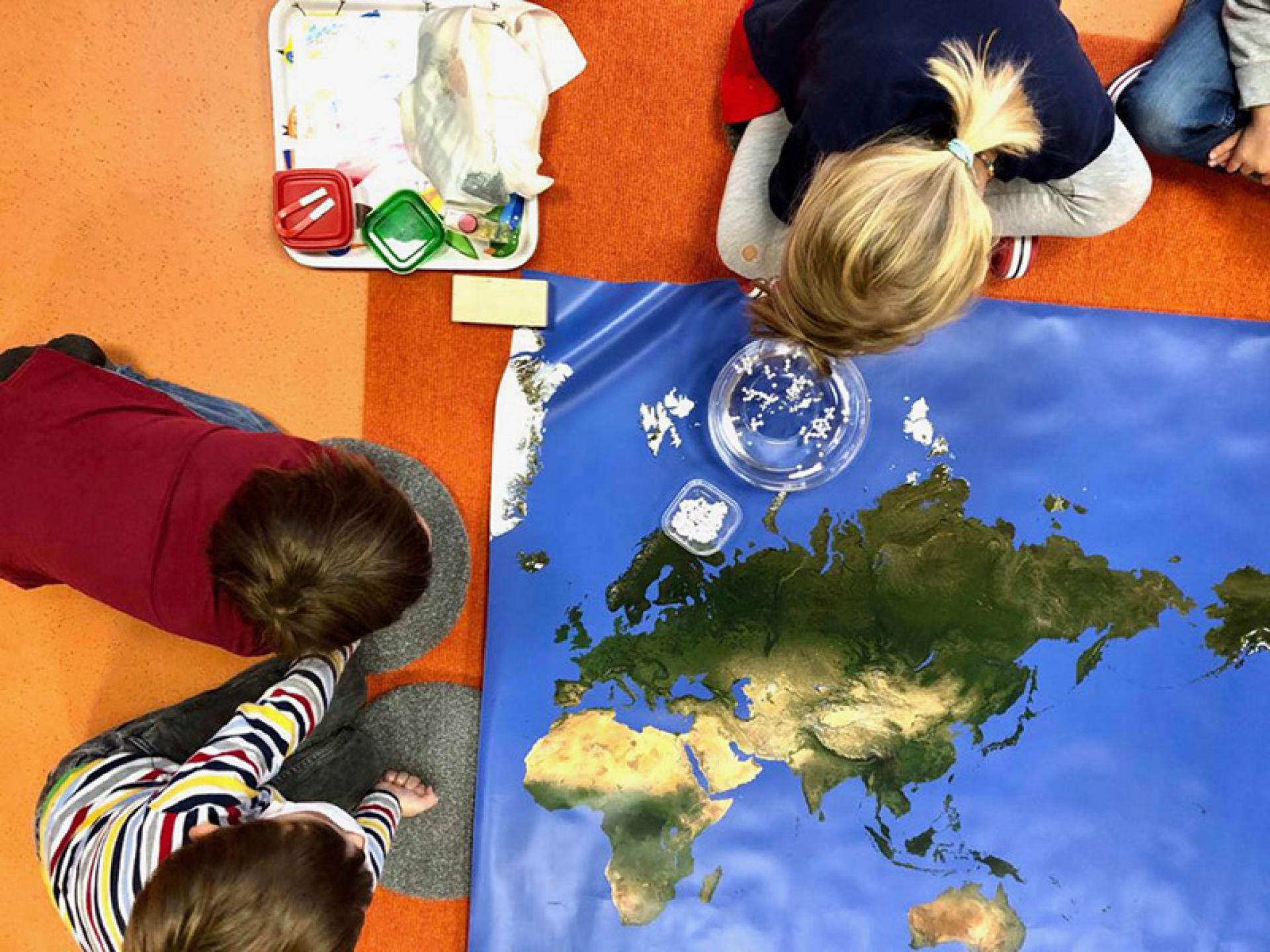Kinder spielen auf dem Boden mit einer Weltkarte und erkunden verschiedene Länder und Kontinente
